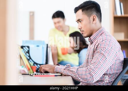 Seitenansicht eines jungen engagierten asiatischen Experten, der an seinem Schreibtisch sitzt, während er im Büro an einem Laptop arbeitet Stockfoto