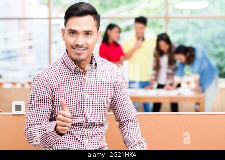 Porträt der jungen asiatischen Mitarbeiter zuversichtlich zeigen, Daumen hoch, während vor ein kreatives Team im Büro posing Stockfoto