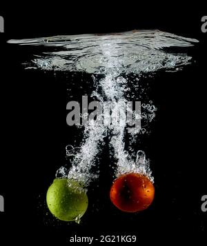 Frische rote Tomaten und gelbe Zitrone, die auf schwarzem Hintergrund ins Wasser fallen Stockfoto