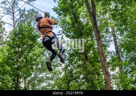 Junge Frau, die bei Screaming Eagle Aerial Adventures im Chattahoochee Nature Center in Roswell, Georgia, unter den Baumwipfeln ziplint. (USA) Stockfoto