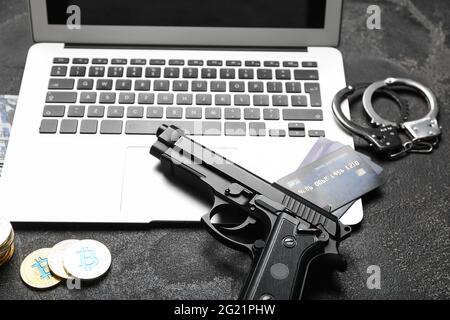 Komposition mit Laptop, Pistole, Handschellen, Kreditkarten und Bitcoins auf dunklem Hintergrund. Hacking-Konzept Stockfoto