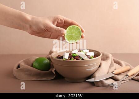 Frau quetscht frischen Limettensaft auf leckere Linsen mit Käse in der Schüssel Stockfoto