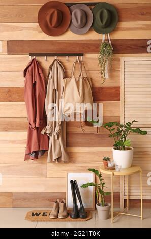 Kleiderbügel mit Kleidung und Hüten an der Holzwand Stockfoto