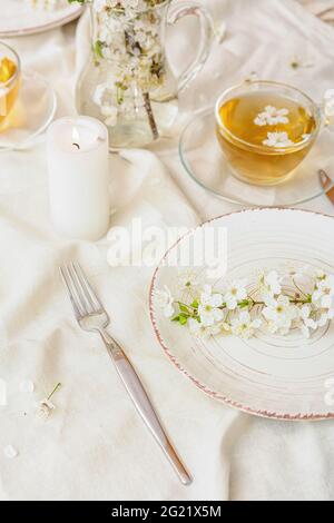 Tischeinstellung mit blühenden Ästen und einer Tasse Tee auf hellem Hintergrund Stockfoto