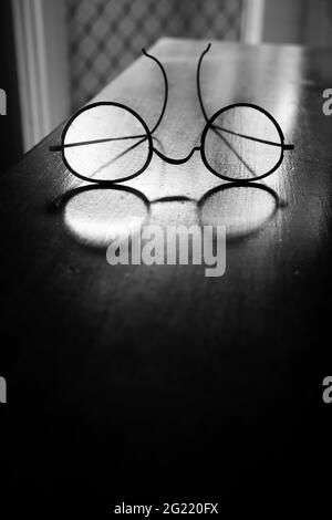 Eine altmodische Vintage-Brille mit Drahtrahmen, durch die Licht auf einem alten schwarzen und weißen Holztisch mit Platz zum Kopieren durchscheint. Stockfoto
