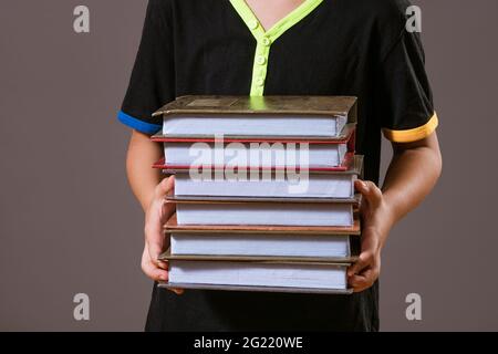 Schuljunge in schwarzem T-Shirt mit einem Stapel Bücher auf grauem Hintergrund Stockfoto