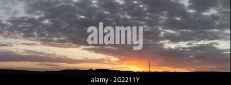 Panorama des Sonnenuntergangs über dunklem Wald. Elektrische Pole auf einem Hintergrund des leuchtend orangefarbenen Sonnenhimmels Stockfoto