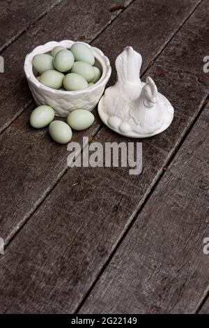 Retro Vintage weiße Keramik oder Porzellan Huhn geformt Eierhalter auf strukturiertem rustikalem Holz Hintergrund mit blauen araucana Hühnereier. Stockfoto