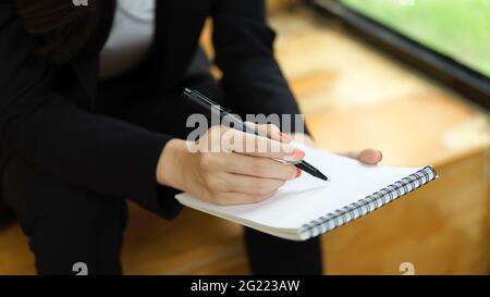 Nahaufnahme einer Geschäftsfrau, die auf einem leeren Notizbuch schreibt, während sie in der Relax-Ecke sitzt Stockfoto