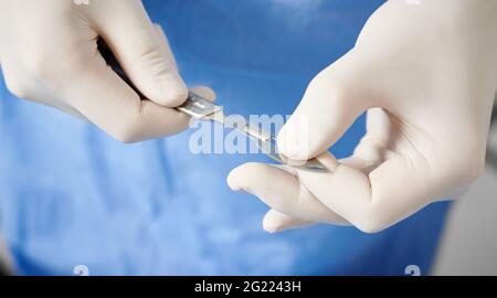 Nahaufnahme der Hände des Arztes, die Skalpell für die plastische Chirurgie vorbereiten. Chirurg mit medizinischem Instrument aus Edelstahl in den Armen mit weißen sterilen Handschuhen. Konzept der Chirurgie und Medizin. Stockfoto