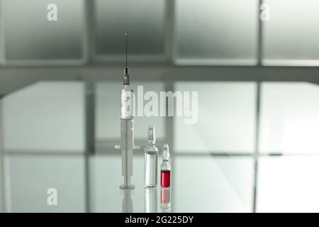 Medikamentenfläschchen und Spritze auf Glastisch im Krankenhauszimmer Stockfoto