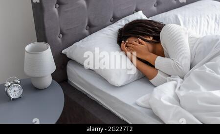 Schwarze Frau weinend, liegend im Bett bedeckendes Gesicht Stockfoto