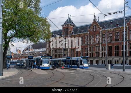 Amsterdam, Niederlande - 19. Mai 2021: Straßenbahnen vor dem Hauptbahnhof in der Innenstadt von Amsterdam mit Pendlern und Menschen warten Stockfoto