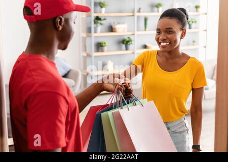 Happy Black Woman Empfängt Einkaufstaschen Von Courier Standing Indoor Stockfoto