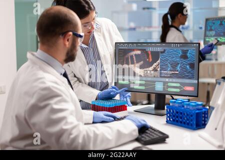 Gruppe von Wissenschaftlern, die in modern ausgestatteten Labor zeigt auf Computer-Desktop. Y zeigt auf Computer-Desktop. Chemiker analysieren die Virusentwicklung mithilfe von Hightech-Technologien für die Behandlungsforschung. Stockfoto