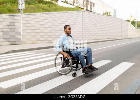 Porträt eines behinderten jungen schwarzen Mannes im Rollstuhl, der die Straße der Stadt überquert, Kopierraum Stockfoto
