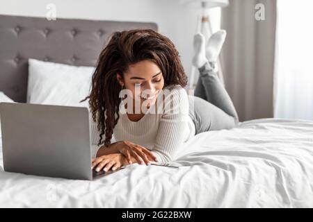 Positive schwarze Frau, die im Bett liegt und eine Textnachricht liest Stockfoto