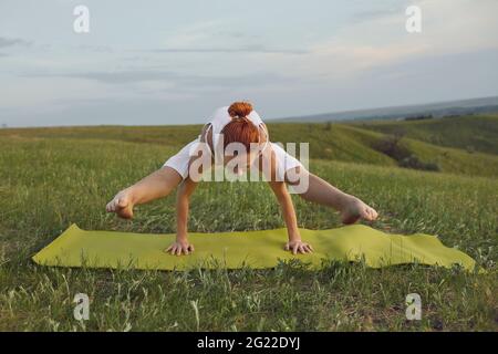 Fit Frau in activewear tun Tittibhasana auch bekannt als Firefly Pose auf Yoga-Matte im grünen Feld Stockfoto