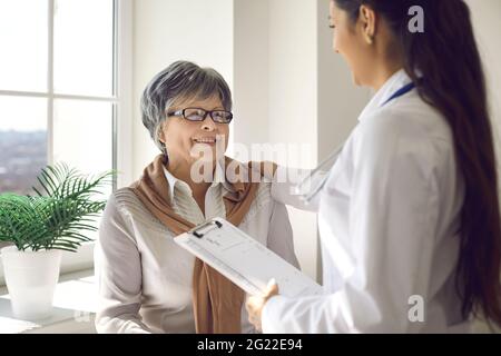 Ältere Frau, die den Arzt anschaut und ihrem Rat mit einem glücklichen Lächeln im Gesicht zuhört Stockfoto
