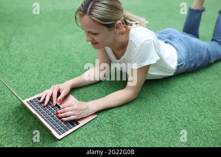 Lächelnde Frau liegt auf einem grünen Rasen mit Laptop Stockfoto