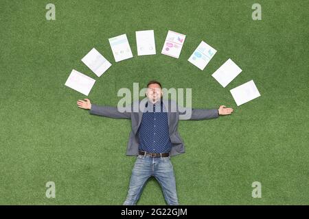 Glücklicher Geschäftsmann liegt auf grünem Rasen in Dokumenten mit Geschäftsdiagrammen Stockfoto