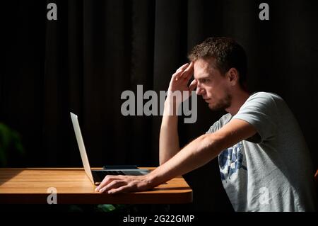 Seitenansicht eines nachdenklichen jungen, gutaussehenden Mannes, der mit einem Laptop arbeitet oder studiert. Konzept des Prozesses Denken über die Arbeit mit modernen Computer. Stockfoto