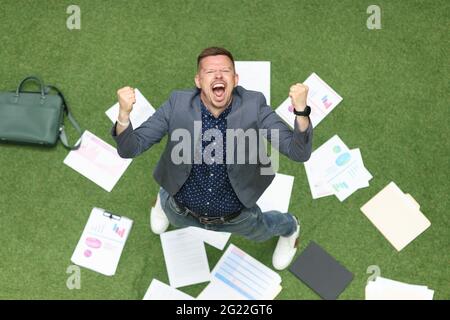 Fröhlicher Mann hebt seine Hände hoch und schreit auf dem Boden liegt Geschäftsgrafik Stockfoto