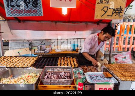 Kyoto, Japan - 21. November 2018: Asiatischer Mann goss Mayonnaise auf Takoyaki in einem kleinen Straßenunterstand beim Festival vor dem Fushimi Inari-Schrein. Stockfoto