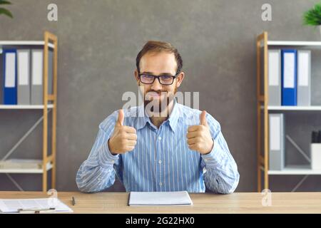 Glücklicher junger Geschäftsmann oder Büroangestellter, der zeigt, dass er mit den Arbeitsergebnissen zufrieden ist Stockfoto