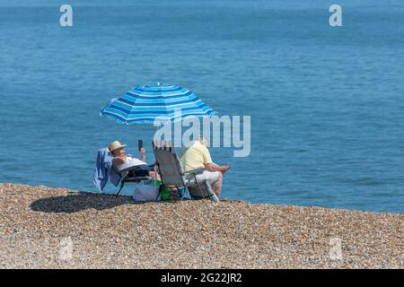 Zwei Personen entspannen an einem Kiesstrand an einem heißen Sommertag in England Stockfoto