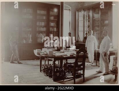 Shop des Deli Courant. Blick auf das Deli Courant Print-Geschäft in Medan, zentral ein Tisch mit neuen Ausgaben, an den Wänden Schränke mit Büchern. Mit ständigen europäischen und javanesischen Mitarbeitern. Teil einer separaten Gruppe von neun Fotos aus dem Jahr 1908 innerhalb der gesamten Gruppe von 49 losen Schwarz-Weiß-Fotos unterschiedlicher Formate über den Verlag und den Druck der Zeitung Deli Courant in Medan im Zeitraum 1885-1947. Stockfoto