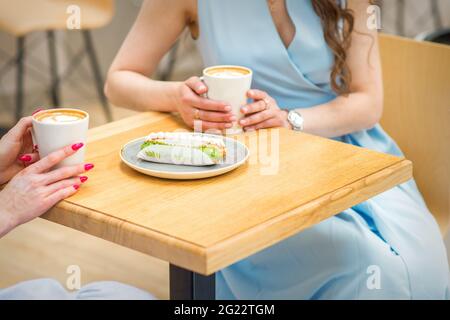 Zwei junge Frauen mit Tassen Kaffee und Kuchenstücken sitzen im Café draußen am Tisch Stockfoto