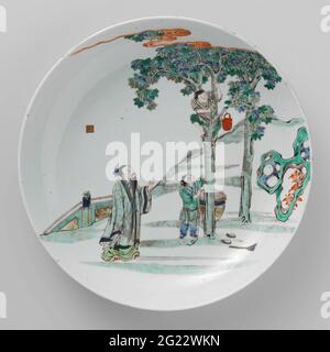 Gericht mit einem Mann und einem Jungen, der einen Jungen in EINEM Baum ansieht. Porzellanskala mit runder Wand, in Unterglasur blau und auf der Glasur blau, rot, grün, gelb, Aubergine gemalt, Schwarz und Gold. Vorne drei Personen in einem eingezäunten Garten: Ein Mann steht neben einem Baum, in den ein Junge geklettert ist, ein zweiter Junge steht unter dem Baum neben einem Topf mit einem Seil in den Händen. Das Seil wird an einen Eimer geklebt, der über einen Ast geschlagen wird. Neben dem Baum sind die Schuhe und der Besen des Jungen im Baum. Über dem Tor eine Dichtung. Unten mit einem Artemisia-Blatt in einem Doppelkreis markiert. Famille Verte. Stockfoto
