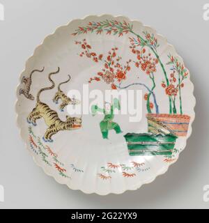Saucer-Dish With Bamboo, Prunus, Tiger and a Chinese Boy. Scale of porcelain with a ribbed wall and lobed edge, painted on the glaze in blue, red, green, yellow, black and gold. On the front a dancing Chinese boy between three tigers on one side and bamboo and prunus branch behind tied up on the other side. Famille Verte in the Japanese Kakiemon style. Stockfoto