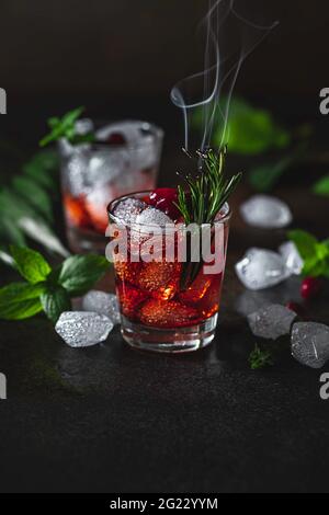 Beerenalkoholischer Cocktaillikör, Wodka, Eis und Rosmarin. Erfrischendes kühles Getränk, Beerenlikör oder roter alkoholischer Cocktail. Selektiver Fokus Stockfoto