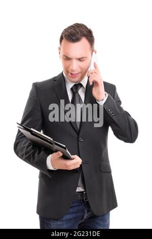 Porträt eines jungen modischen Geschäftsmannes, der auf ein Clipboard schaut und auf einem Mobiltelefon spricht, besorgt, nachdenklich, gestresst, ernst aussieht: Stockfoto