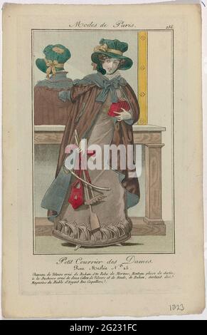 Petit Courrier des Ladies, 1823, Nr. 186: Chapeau de Velours (...). Stehende Frau mit einem Hut aus Samt, verziert mit einem goldfarbenen Band auf dem Kopf. Sie trägt eine Rolle aus Merinowolle. Plissierter Satinmantel mit Kapuze, 'à la Duchesse' verziert mit zwei Samtkragen und Schleifen aus Band, zu den 'Magasins du Diable d'Argent Rue Coquilliere'. Eine Reihe von Büchern in der linken Hand. Gartengeräte, Beutel und kleiner Säbel (?) In der rechten Hand. Handschuhe. Ein Spiegel hinter ihr. Druck aus dem Modemagazin Petit Courier des Ladies (1821-1868). Stockfoto