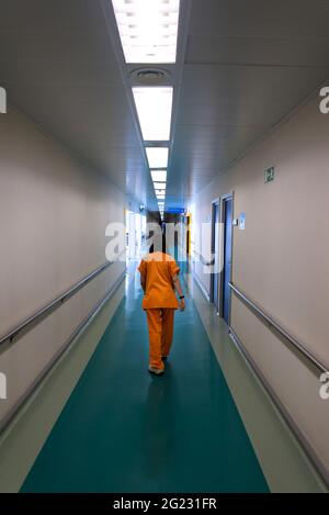 Ein junger Arzt von hinten in orangefarbener Arbeitsuniform, der einen Krankenhauskorridor entlang läuft. Vertikales Bild Stockfoto
