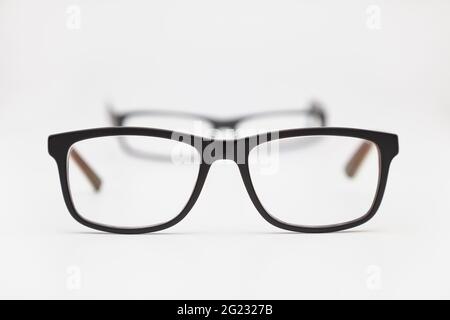 Zwei Paar Brillen auf einer weißen Oberfläche. Die engsten sind im Fokus und die anderen sind nicht im Fokus. Der Hintergrund ist weiß. Stockfoto