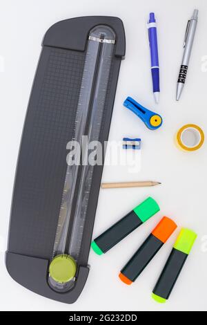 Büro-Guillotine, Textmarker, Bleistift, Stifte, Bleistiftspitzer, Locher und doppelseitiges Klebeband auf weißem Hintergrund. Stockfoto