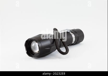 Schwarze Laterne auf weißem Hintergrund. Die Taschenlampe ist ausgeschaltet, sie hat einen Riemen, um sie zu halten, und einen Haken, um sie an der Taille zu befestigen. Stockfoto