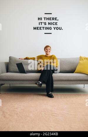 Frau, die in der Bürolobby sitzt und die Kamera anlächelt. In der Lobby sitzt eine Unternehmerin. Stockfoto