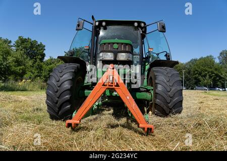 Niedriger Winkel Ansicht des grünen Traktors im Heufeld im Sommer mit offenen Türen und tiefblauem Himmel. Stockfoto