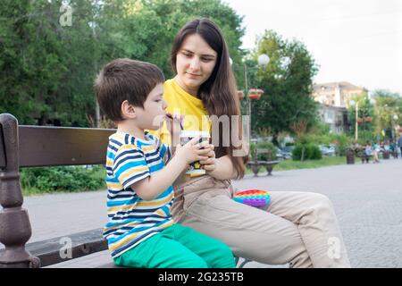 Mama und kleiner Sohn trinken im Park in der Stadt Kakao. Kakao oder Milchshake im Sommer im Freien, Familienurlaub. Stockfoto