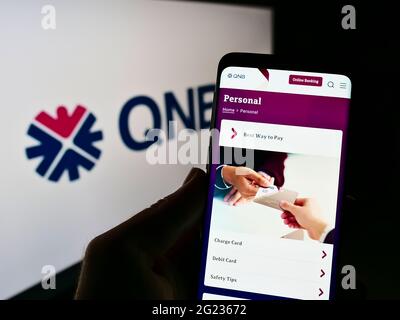 Person, die Smartphone mit der Webseite des Finanzunternehmens Qatar National Bank (QNB) auf dem Bildschirm vor dem Logo hält. Konzentrieren Sie sich auf die Mitte des Telefondisplays. Stockfoto