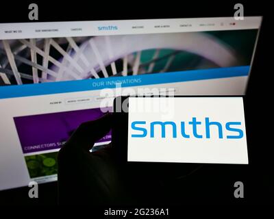 Person, die ein Mobiltelefon mit dem Logo des britischen Ingenieurunternehmens Smiths Group plc auf dem Bildschirm vor der Webseite hält. Konzentrieren Sie sich auf die Telefonanzeige. Stockfoto