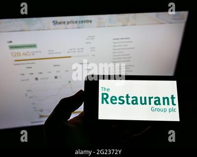 Person, die ein Smartphone mit dem Logo des britischen Gastronomieunternehmens The Restaurant Group plc auf dem Bildschirm vor der Website hält. Konzentrieren Sie sich auf die Telefonanzeige. Stockfoto