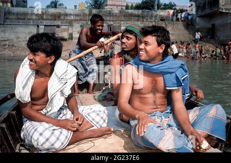 Lachende junge Männer in Dhotis werden auf einem lokalen Flusstaxi-Boot über den Buriganga River, Dhaka, Bangladesch, gerudert. Stockfoto