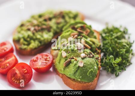 Veganes Avocado-Sandwich mit Tomaten und Microgreens auf einem weißen Teller Stockfoto