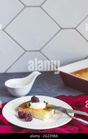 Hüttenkäse-Auflauf auf einem weißen Teller und Tee in einer burgunderroten Tasse auf grauem Hintergrund Stockfoto